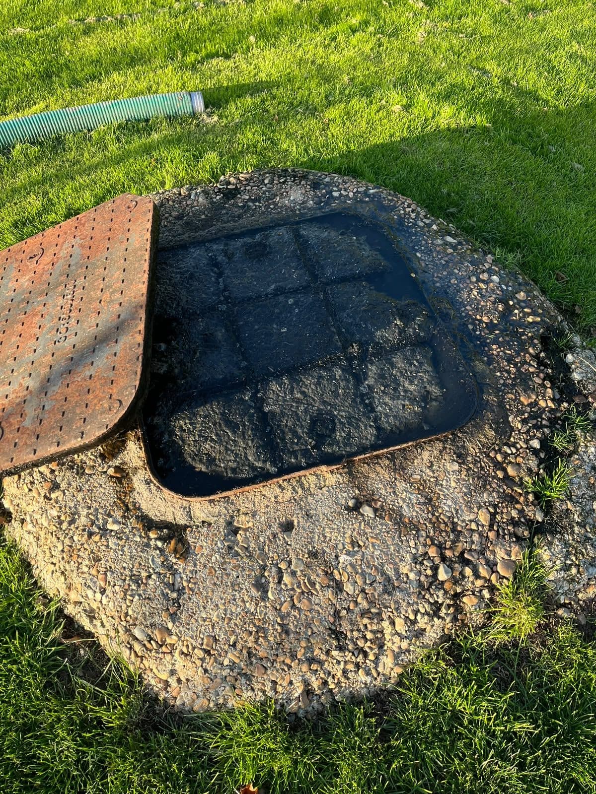 Square access cover lifted clear of a round chamber ready for emptying