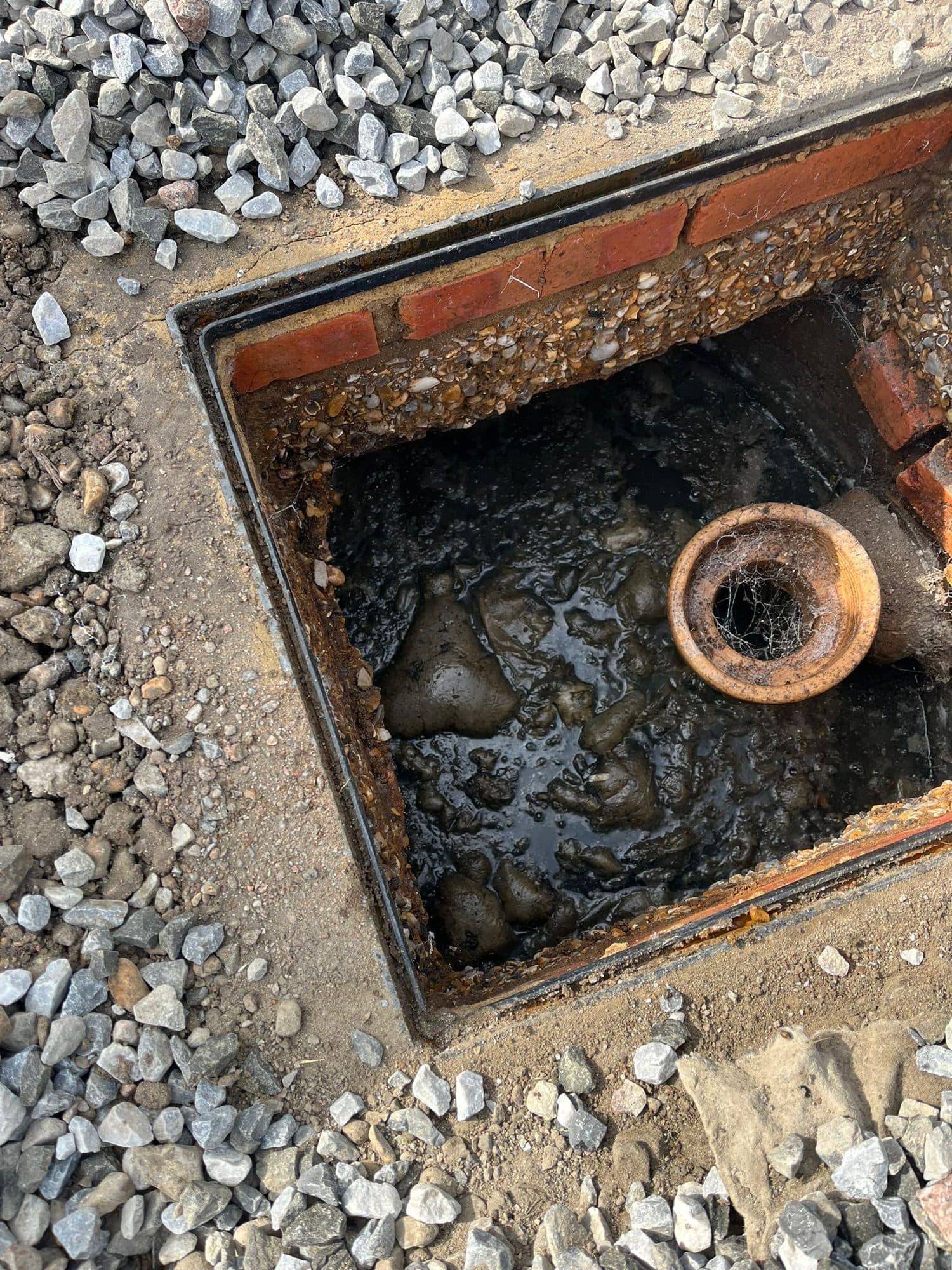 Brick inspection chamber surrounded by gravel with the clay pipe and waste level visible