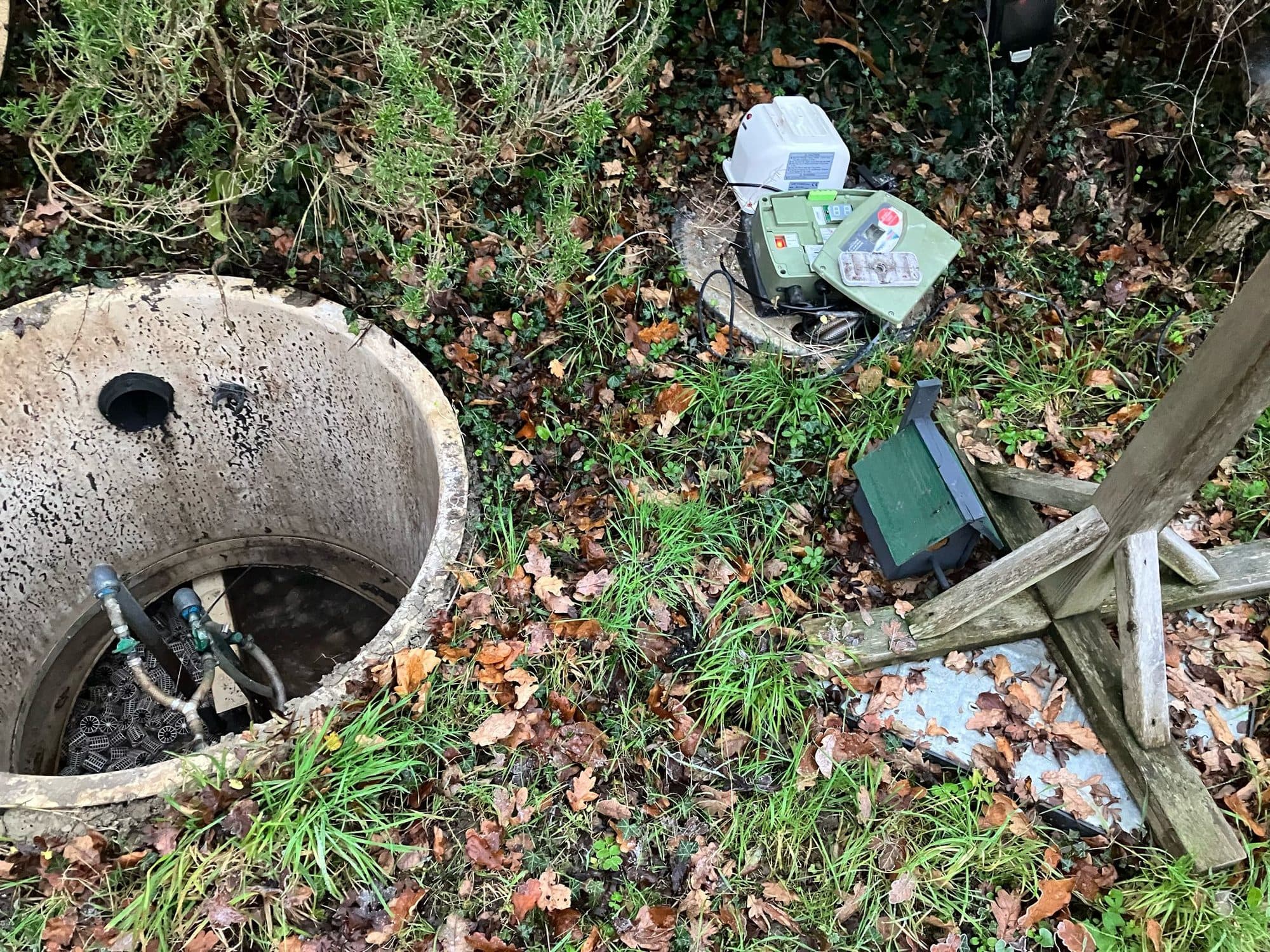 Open circular tank chamber with the treatment plant control panel and alarm unit on the ground alongside