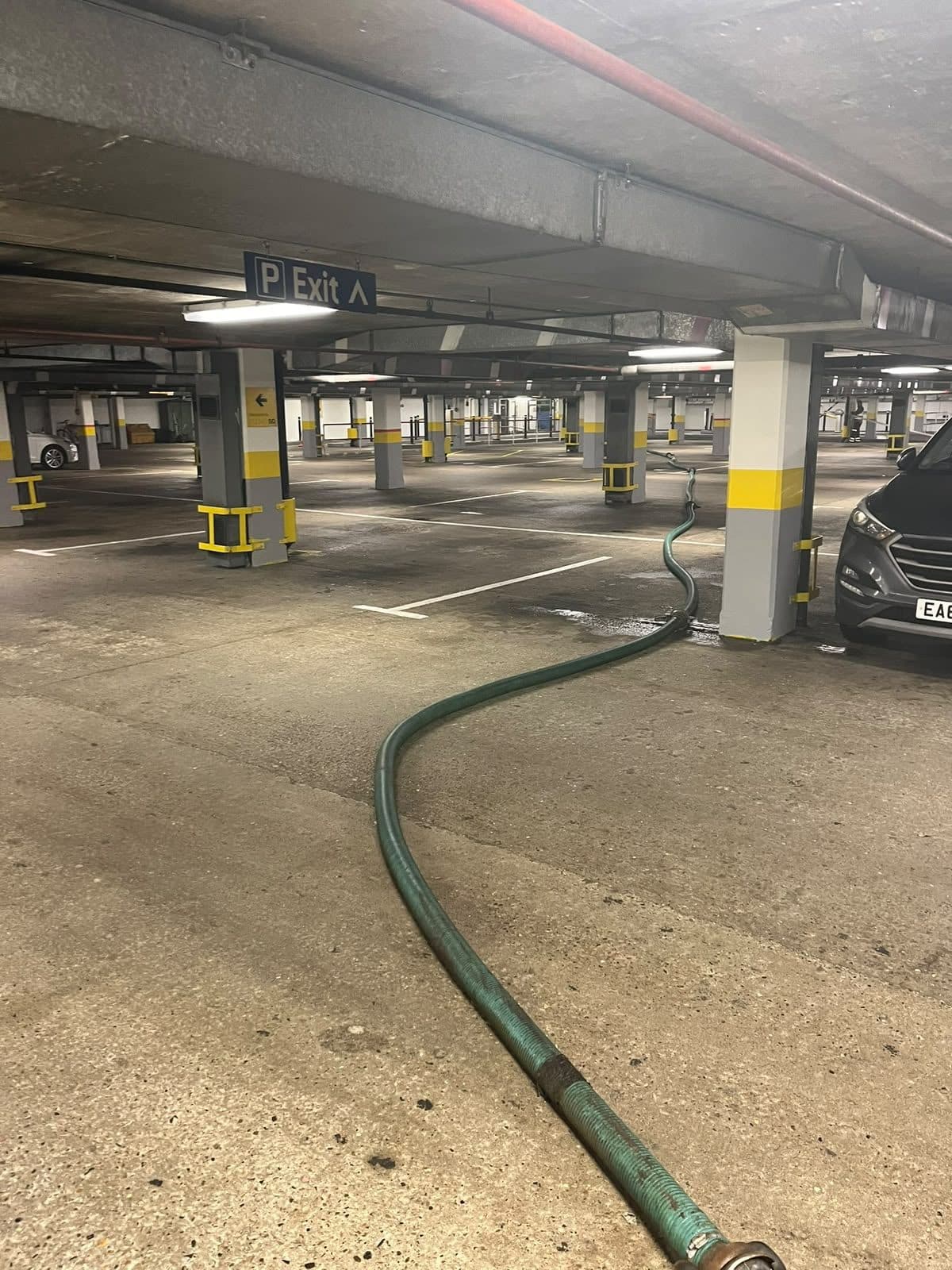 Suction hose run between parked cars across the deck of a multi storey car park