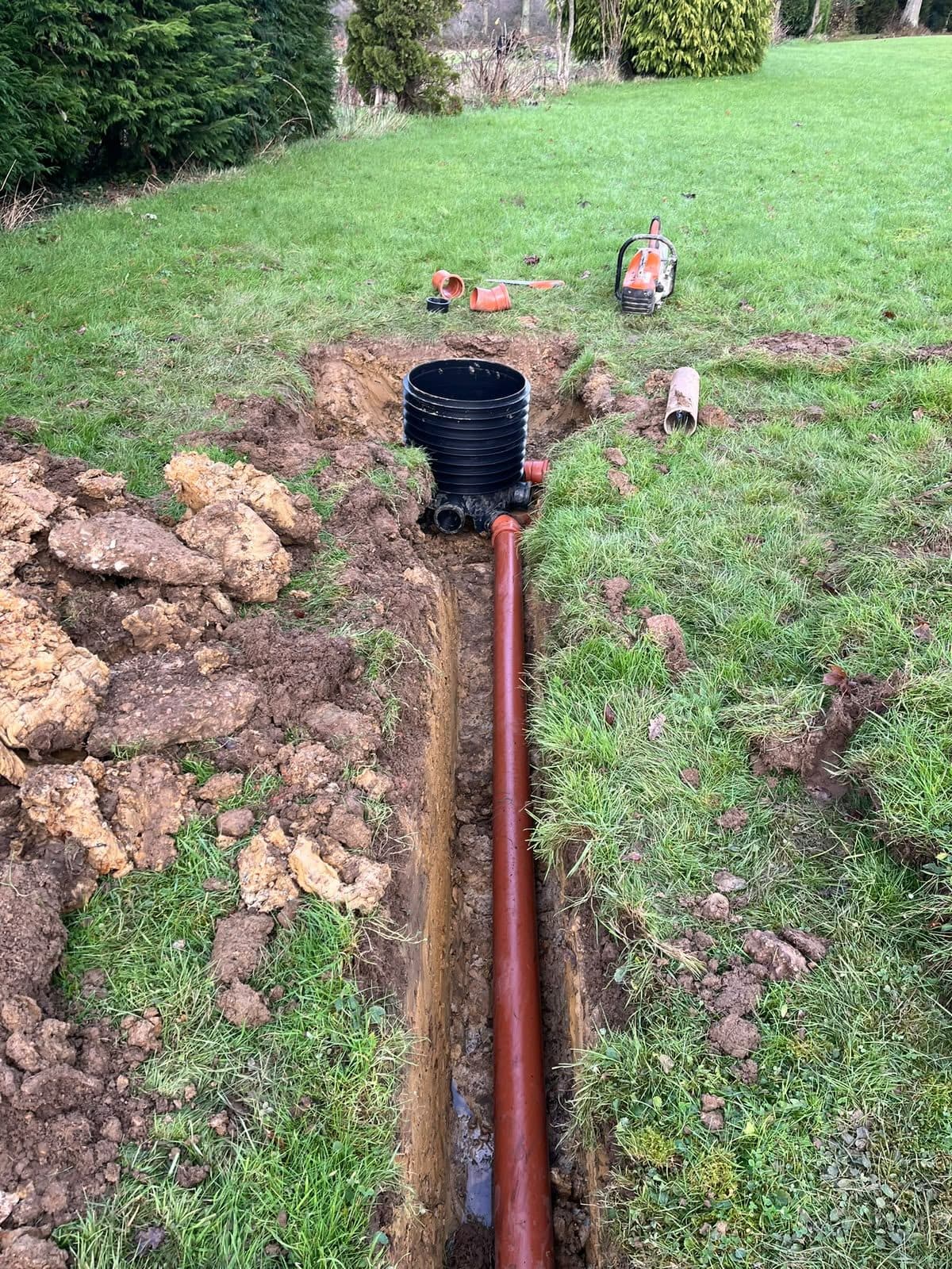 New pipe run laid in an open trench across a lawn during a tank installation
