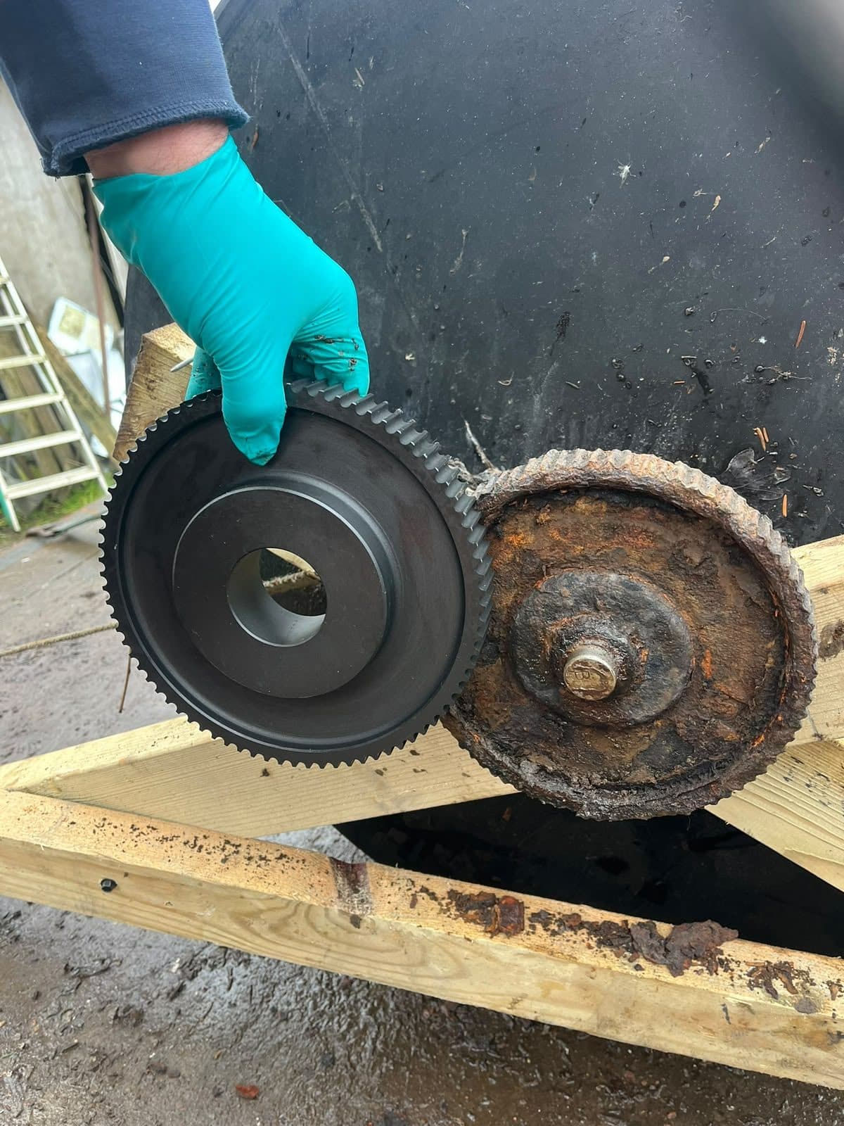 Gloved hand holding a new drive sprocket beside the worn one it replaces on a treatment plant