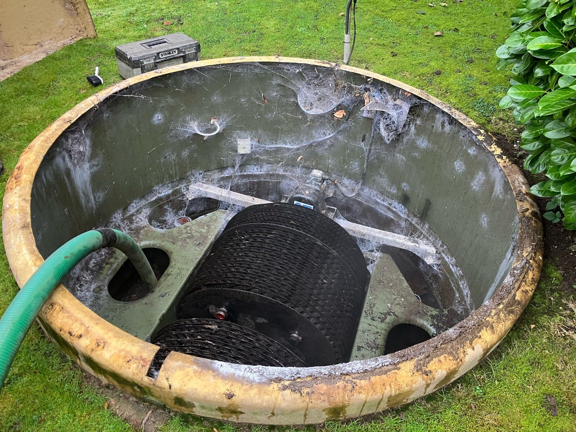 Open concrete treatment plant chamber in a garden with the green suction hose lowered inside